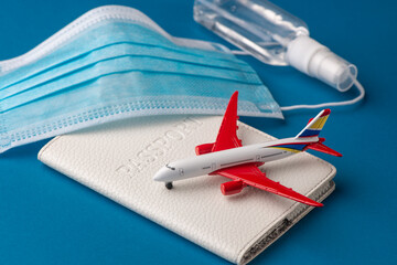 Plane toy, sanitizer spray, face mask and passport on blue background