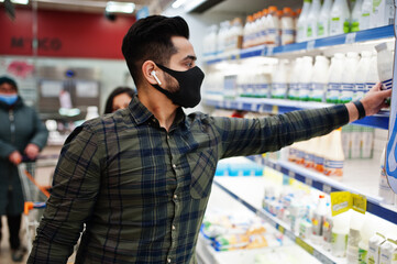 Asian man wear in protective face mask shopping in supermarket during pandemic. Taking milk products from fridge.