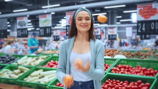 cheerful woman juggling with yellow tomatoes in supermarket