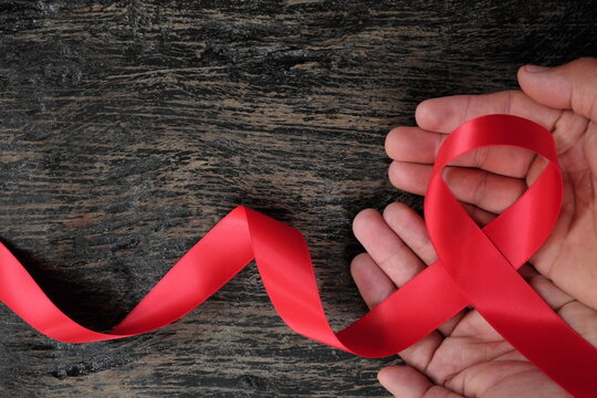 Top view of male hand holding red ribbon on dark wood background. AIDS, HIV, heart disease and stroke awareness concept.
