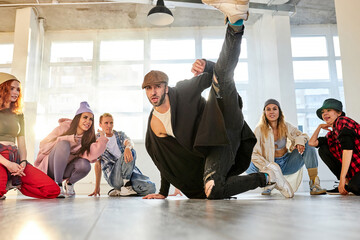 Fototapeta premium male dancer performing break dance or hip-hop in studio, group of professinal dancers next to him support, look at him