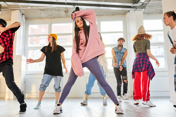 Naklejka premium group of young dancers performing a common choreography in modern dance studio, wearing trendy clothes