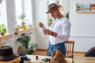 craftsman tailor sews fabric for the inside of the handmade hat in workshop, using thread and needle