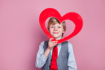 Valentines day. Funny little boy posing with heart on pink background