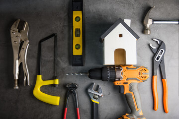 Wooden white house toy and construction tools on Gray-black cement floor background with copy space.Real estate concept, New house.Home repair concept