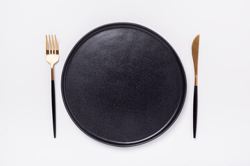 Black ceramic plate, fork and knife on white background. Top view - Image