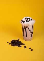Milkshake with coffee topping. Iced chocolate with whipped cream on a yellow background. Coffee beans
