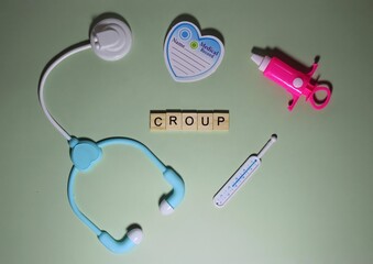 CROUP word made from wooden cube on light green background surrounded by set of toy medical...