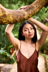 brunette woman in silk dress posing near tree in the garden, she is smiling at camera