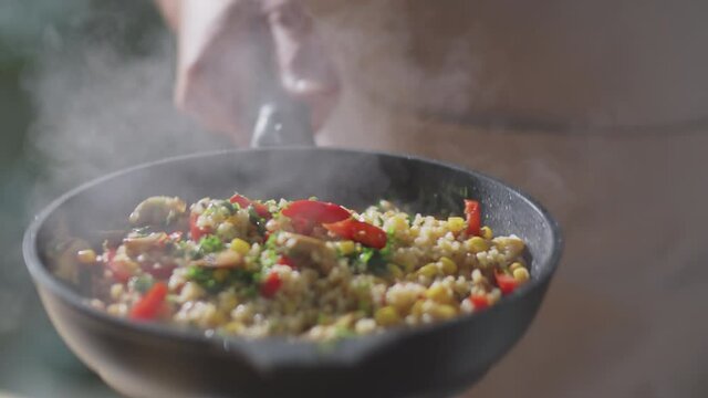 Close up shot of unrecognizable male chef tossing food on hot frying pan while cooking in kitchen