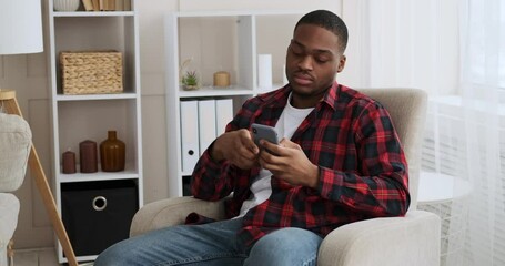 Frustrated man throwing away mobile phone sitting on armchair at home