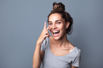 Beautiful joyful woman showing two fingers over gray background