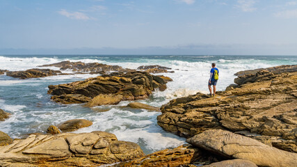Fototapeta na wymiar Hiker enjoying the view along a rocky stretch of coastline in the Tsitsikamma National Park, South Africa.