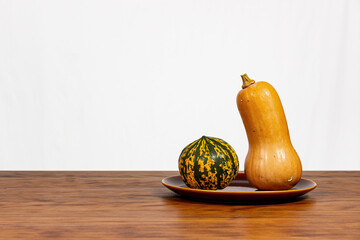 Still life of two pumpkins on an earthenware plate. Wood and white background.