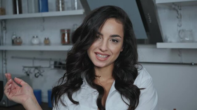 seductive woman in white shirt touching hair and looking at camera in kitchen