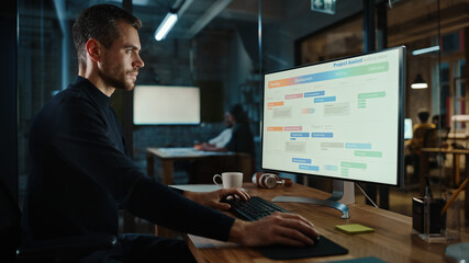 Young Handsome Project Manager Working on a Marketing Presentation on Desktop Computer in Busy Creative Office. Male Specialist is Implemeting Business Strategy Points Into the Keynote.