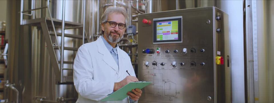 Food technologist in white lab coat in a brewing factory. Male food technologist looking at camera and smiling. Factory, brewery concept.