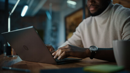 Handsome Black African American Man Having an Online Conversation on a Laptop Computer in Creative Office Environment. Happy Male is Browsing Social Media and Replying to Friends in Messenger.