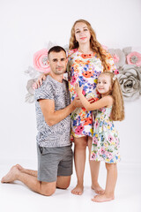 Portrait of a happy family father, pregnant mother, little daughter having fun together isolated over white with floral background