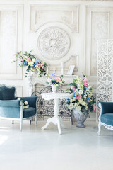 Bright luxury white and blue colored interior living room with flowers in vases. the walls are decorated with baroque ornaments