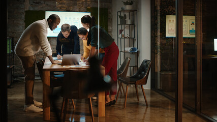 Diverse Multiethnic Team are Having a Conversation in a Meeting Room Behind Glass Walls in a Creative Office. Colleagues Lean On a Conference Table and Discuss Business, App User Interface and Design.