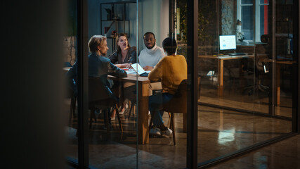 Young Creative Team Meeting with Business Partners in Conference Room Behind Glass Walls in an Agency. Colleagues Sit Behind Conference Table and Discuss Business, App User Interface and Design.