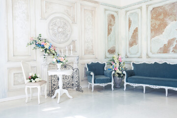 Bright luxury white and blue colored interior living room with flowers in vases. the walls are decorated with baroque ornaments