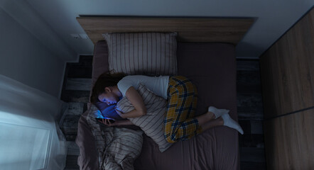 Top view of one woman in bed at night looking at her smartphone, female insomnia problem, woman can...