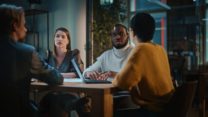 Young Creative Team Meeting with Business Partners in Conference Room Behind Glass Walls in an Agency. Colleagues Sit Behind Conference Table and Discuss Business, App User Interface and Design.