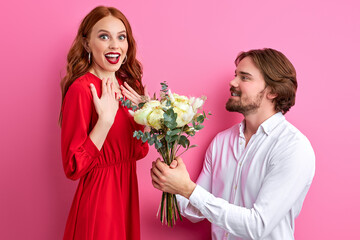 man with boquet of flowers having date with his girlfriend, redhead female is in shock, happy. isolated pink background