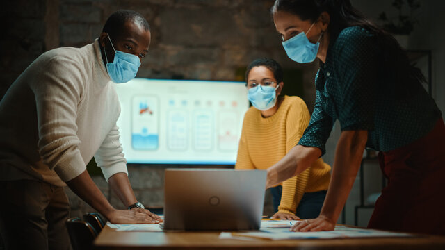 Diverse Multiethnic Team Wearing Face Masks During A Meeting Room Conversation Behind Glass Walls In Creative Office. Social Distancing Restrictions Concept In Work Place During Coronavirus Pandemic.