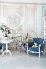 Bright luxury white and blue colored interior living room with flowers in vases. the walls are decorated with baroque ornaments