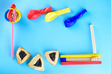 Hamantaschen cookies or hamans ears, wood colorful noisemakers and balloons for Purim celebration jewish carnival holiday on blue background.Top view.Flat lay. Copy space.