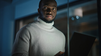 Handsome Black African American Male is Standing in Meeting Room Behind Glass Walls with a Laptop...