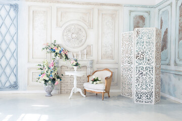 Bright luxury white and blue colored interior living room with flowers in vases. the walls are decorated with baroque ornaments