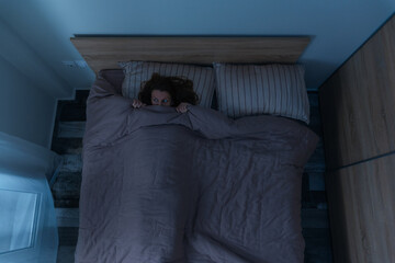 Top view of scared woman alone in bed at night. - obrazy, fototapety, plakaty