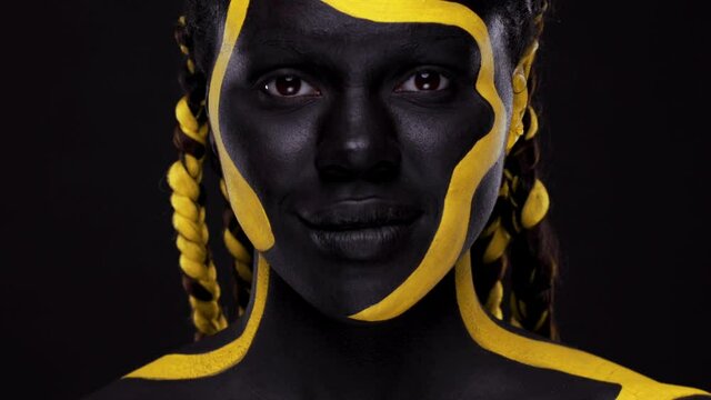 Face art. Woman with black and yellow body paint. Young african girl with colorful bodypaint. An amazing afro american model with yellow makeup. Closeup face.