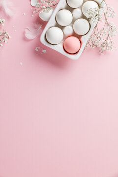 Easter eggs in white ceramic holder and flowers on pink background