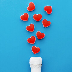 Champagne bottle and heart shaped jelly candies on blue background.