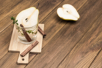 Refreshing pear drink, cinnamon stick and thyme sprig in glass. Slice of pear on table