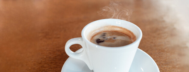Coffee in a cafe on a wooden table. Drink with steam, smoke. Beautiful blurry background with sideways. Sunlight, interior. Delicious Hot Americano Banner