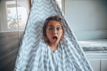 Scared little girl sitting in a tent at home.