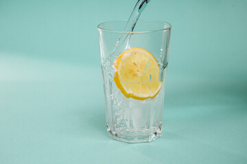 A glass of water with ice and lemon, in which pour sparkling water on a pastel background. Place logo