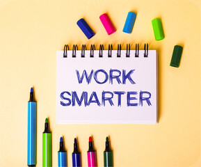 The words WORK SMARTER written in a white notebook on a beige background near multi-colored markers