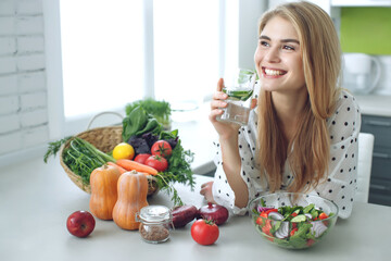 Woman on a diet. Young and happy woman eating healthy salad sitting on the table with green fresh ingredients indoors. High quality photo - 408763500