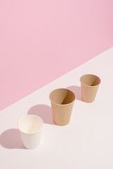 Trending colors. Design of paper cups on white table on pink background. Ecology, environmental pollution by plastic, waste recycling concept. Copy space