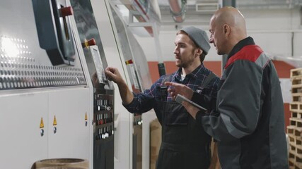 Medium slow-motion footage of two caucasian men in coveralls working at polyethylene production factory setting parameters for machine equipment looking at digital tablet with data - Powered by Adobe