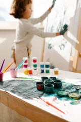 Child painting her hand with paint and paintbrush. Art therapy for children.