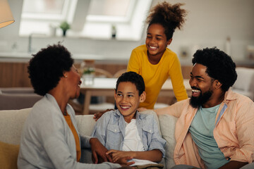 Afro parents and their children are socializing while sitting on the sofa in the living room