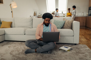 Obraz premium Black man with earphones sitting on the floor and using laptop